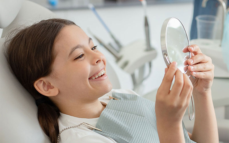 Bambina si guarda allo specchio e ride dal dentista